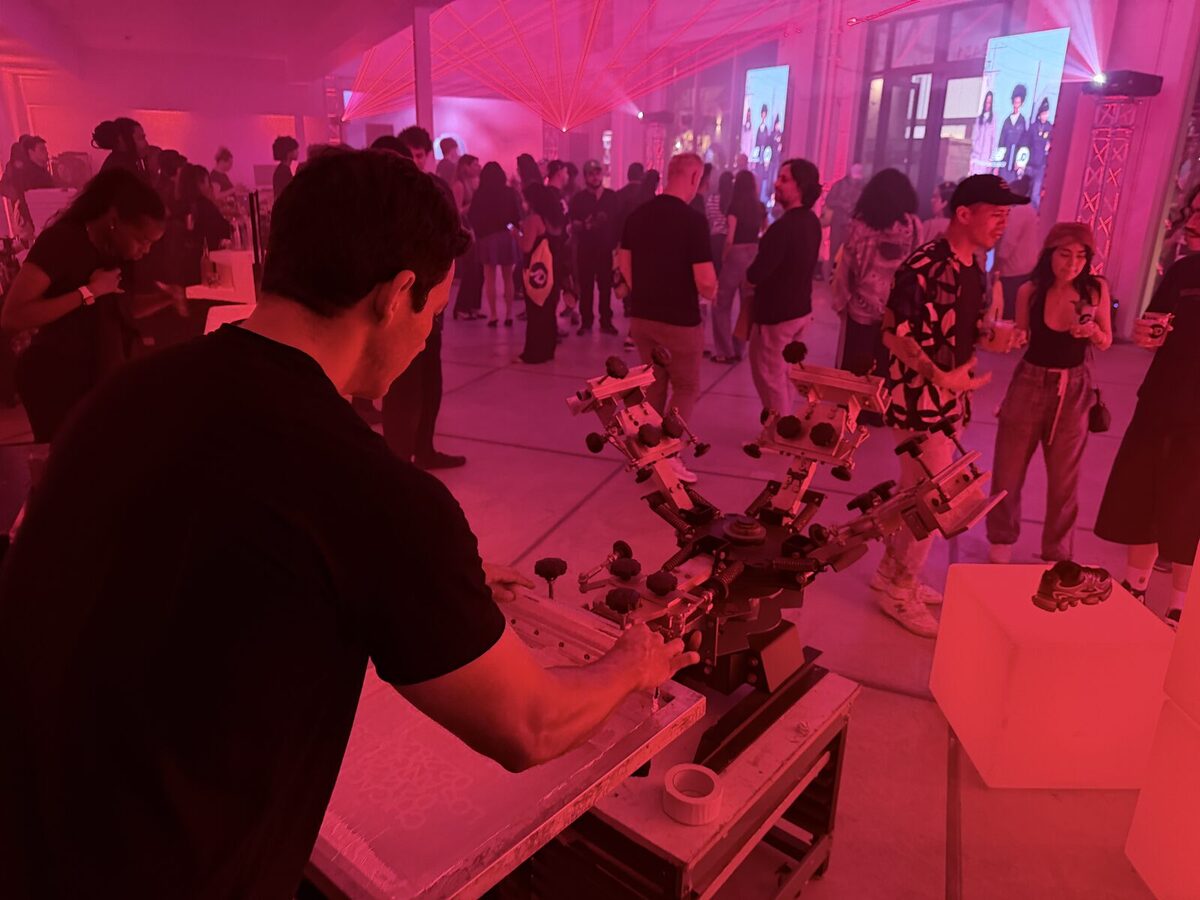 A printer working a carousel press at a night brand activation bathed in red light, with a crowd and laser beams filling the room behind
